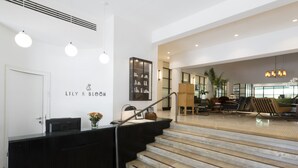 A reception area with a black counter, a staircase, and a seating area with a sofa and chairs. - Lily & Bloom Hotel (Tel Aviv)