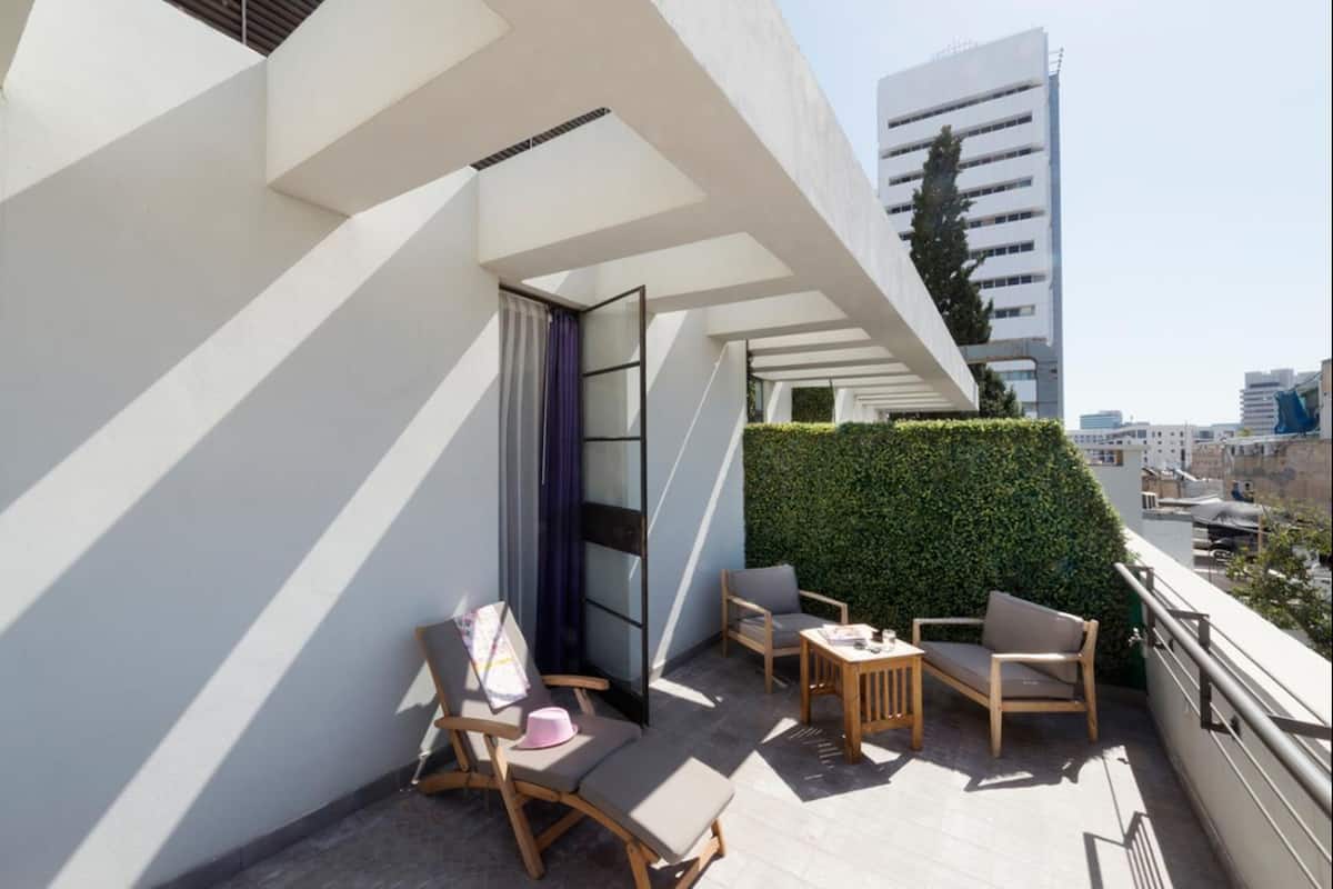 A modern balcony with a seating area, a glass door, and a view of a cityscape.