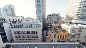 A rooftop terrace with multiple wooden lounge chairs and tables, surrounded by high-rise buildings with balconies and terraces. - Lily & Bloom Hotel (Tel Aviv)