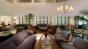 A spacious lobby with a high ceiling, a central seating area with sofas and chairs, a chandelier, and a large window providing natural light. - Lily & Bloom Hotel (Tel Aviv)