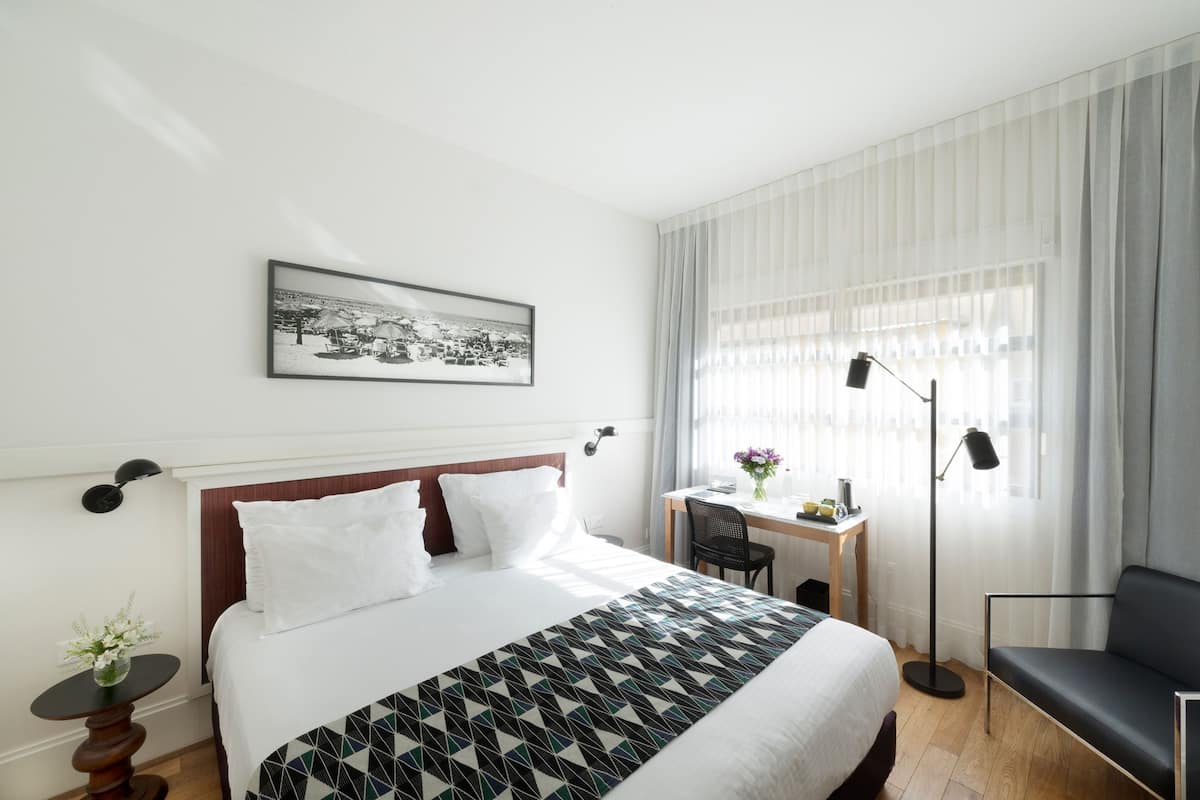 A hotel room with a large bed, a desk, a chair, a lamp, and a picture on the wall.