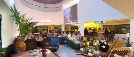A spacious lobby with seating areas, a bar, and a large screen displaying a movie scene.