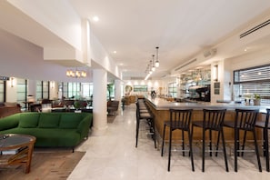 A modern interior with a green sofa, a bar area with stools, and a kitchen in the background. - Lily & Bloom Hotel (Tel Aviv)