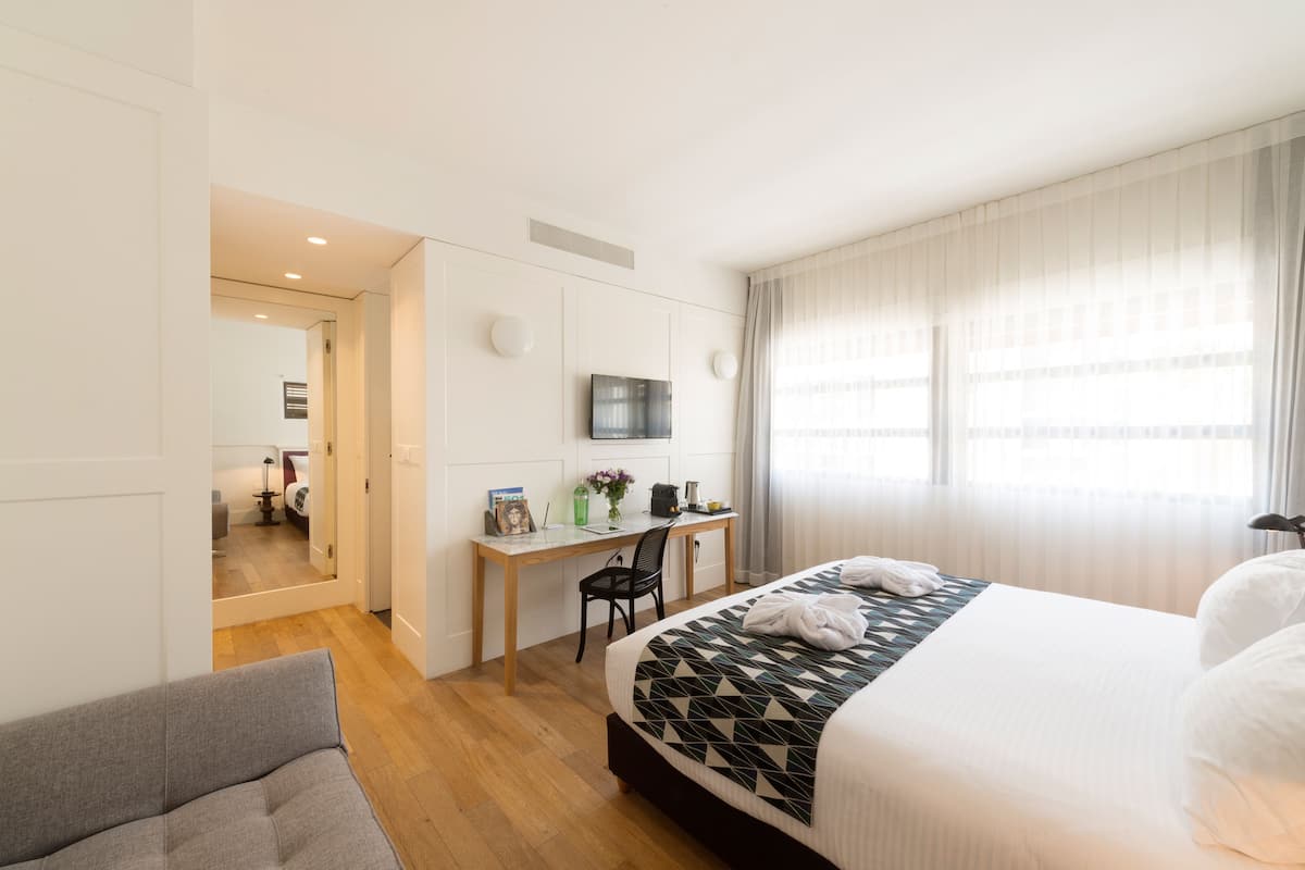 A hotel room with a bed, a desk, a chair, a TV, and a window with curtains.