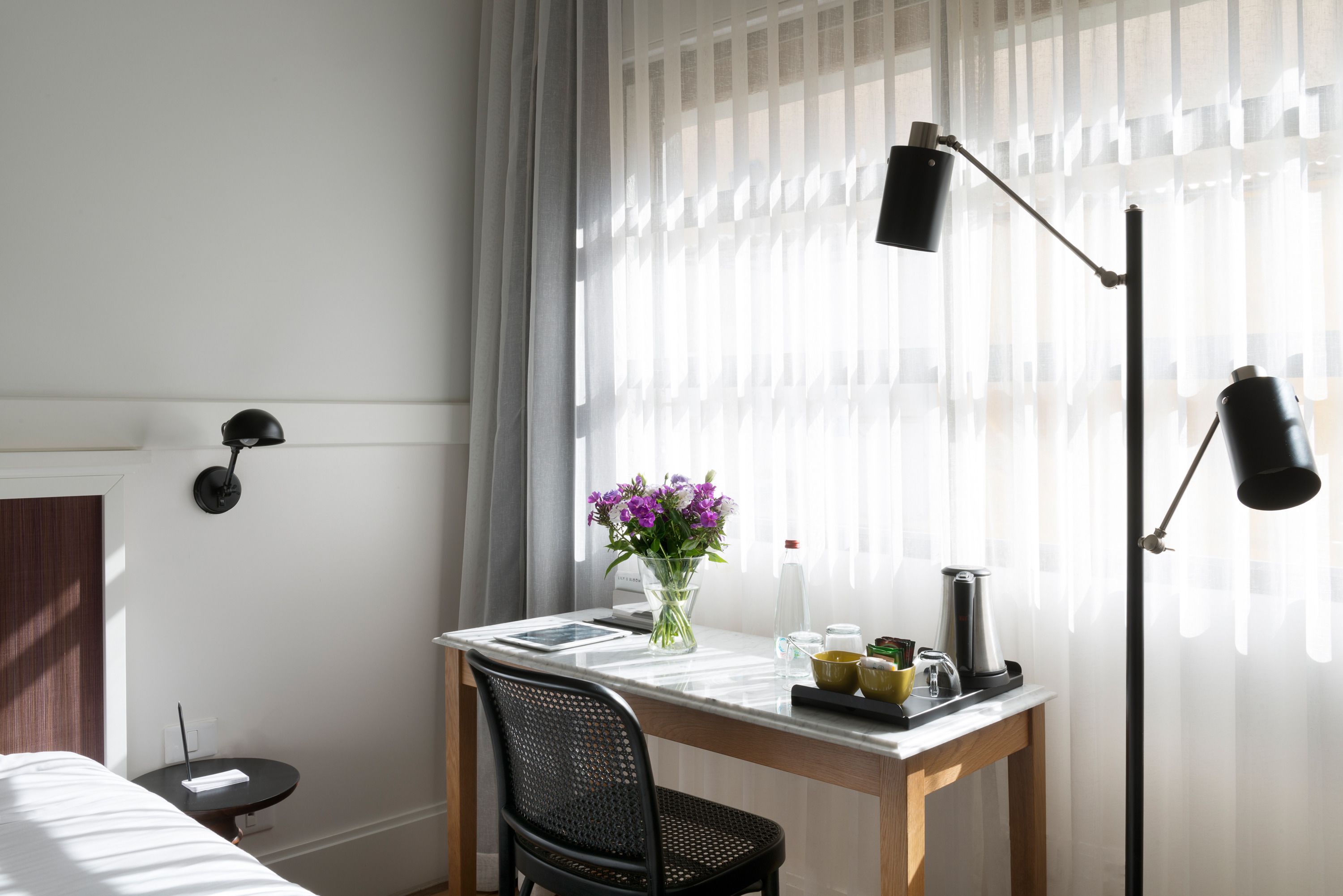 Habitación de hotel con cama, escritorio con un florero, cafetera y lámpara.