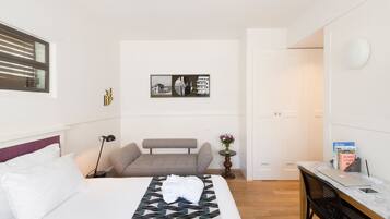 A hotel room with a bed, a sofa, a desk with a laptop, and a wall-mounted artwork.