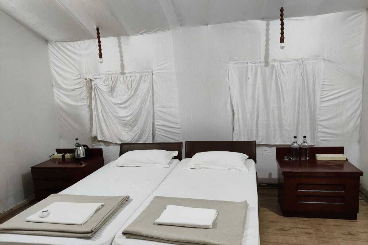 A room with two single beds, wooden nightstands, and a small desk with a chair.