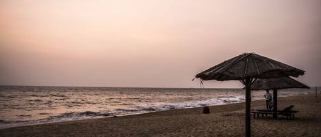 A beach with a thatched umbrella and benches.