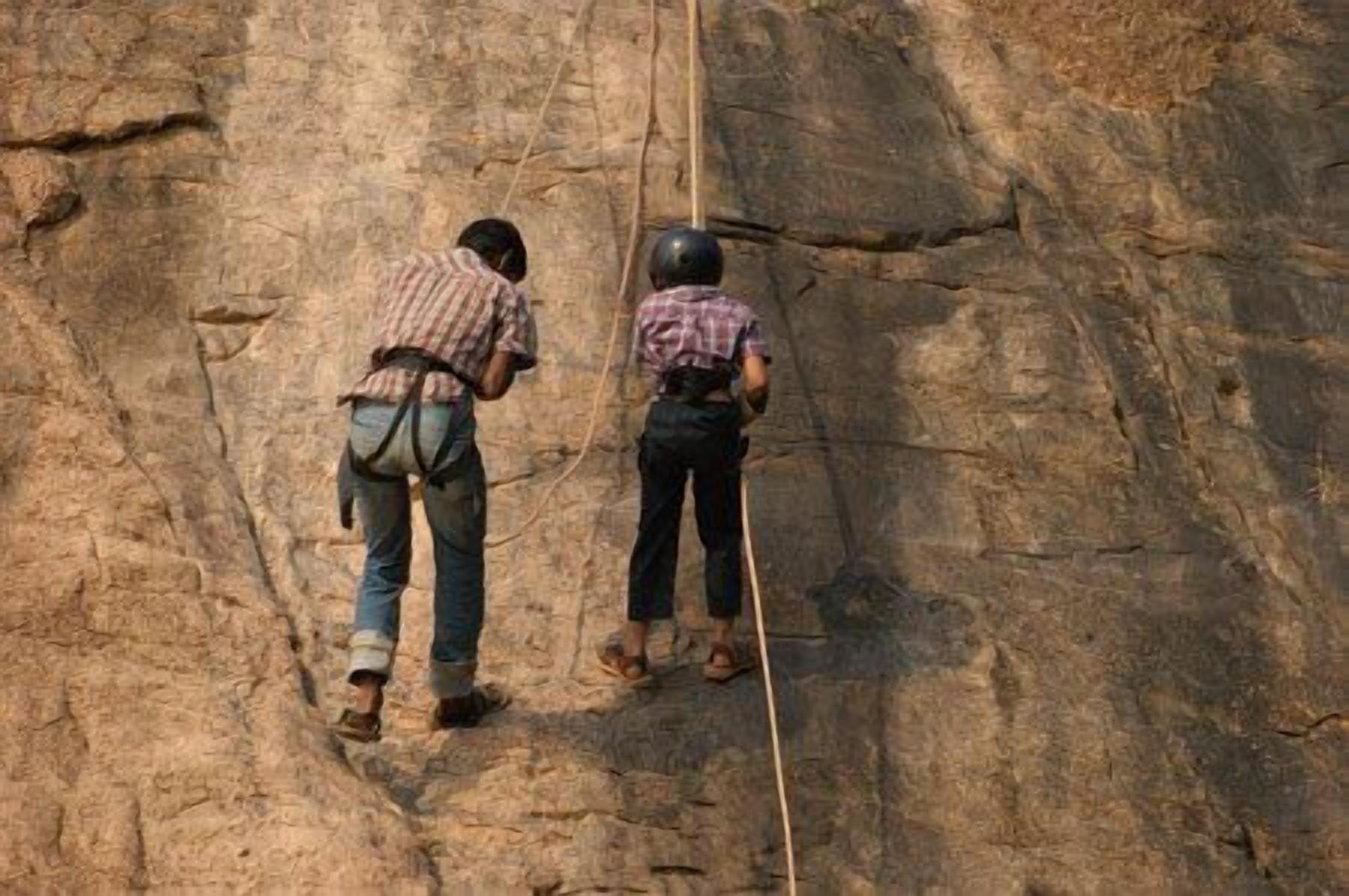 Two individuals climbing a rocky surface with a rope.