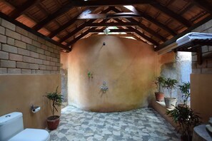 A bathroom with a brick wall, a tiled floor, a wooden ceiling, and several potted plants. - Sai Vishram Beach Resort Byndoor (Kundapur)