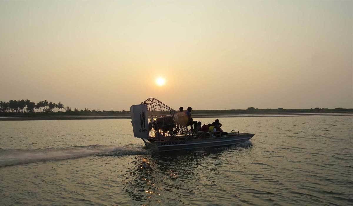 A boat with passengers and a motorized outboard, moving on calm water during sunset.
