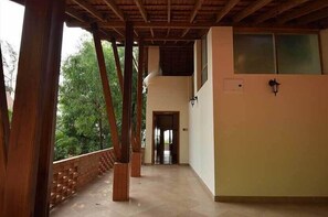 A covered corridor with wooden beams, a brick wall, and a door leading to another room.