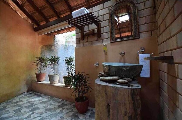 A rustic bathroom with a stone sink, wooden shelf, and potted plants. - Sai Vishram Beach Resort Byndoor (Kundapur)