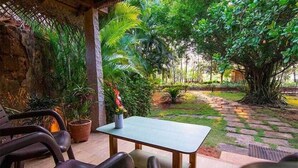 Un espace extérieur aménagé avec une table et des chaises, entouré d’une végétation luxuriante et bordé d’un sentier en pierre.