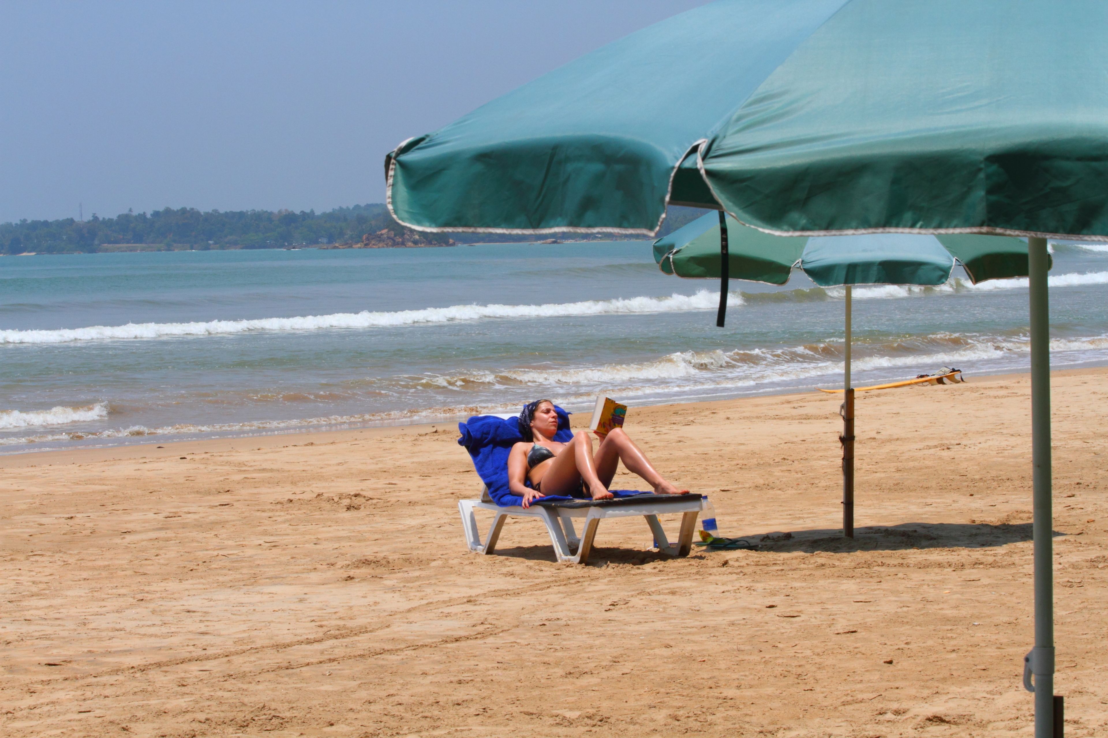 A beach scene with a person relaxing under a green umbrella.