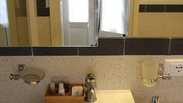 Un baño con lavamanos blanco, un espejo, toallero y dispensador de jabón.