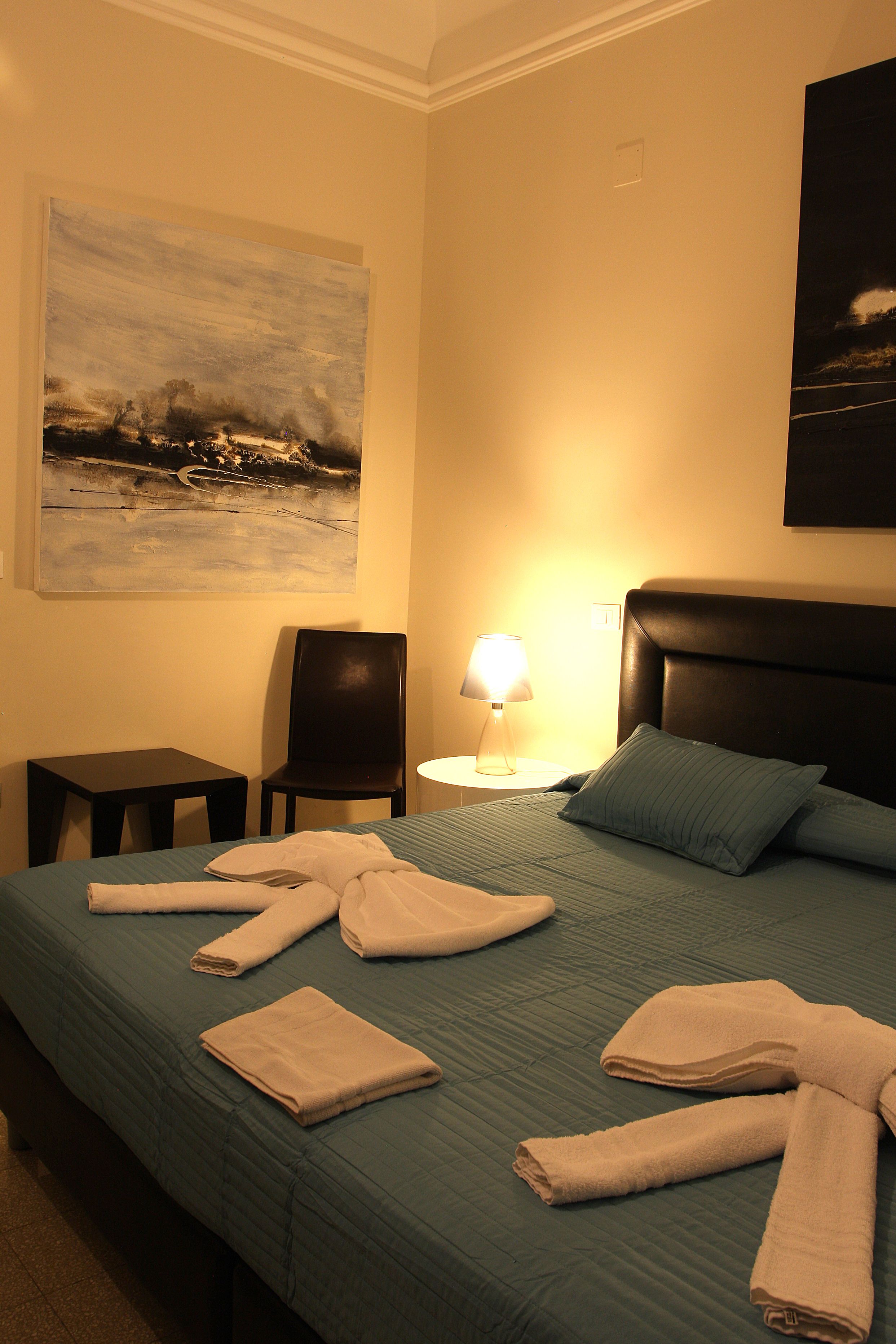 A hotel room with a bed, a chair, a lamp, and a painting on the wall.