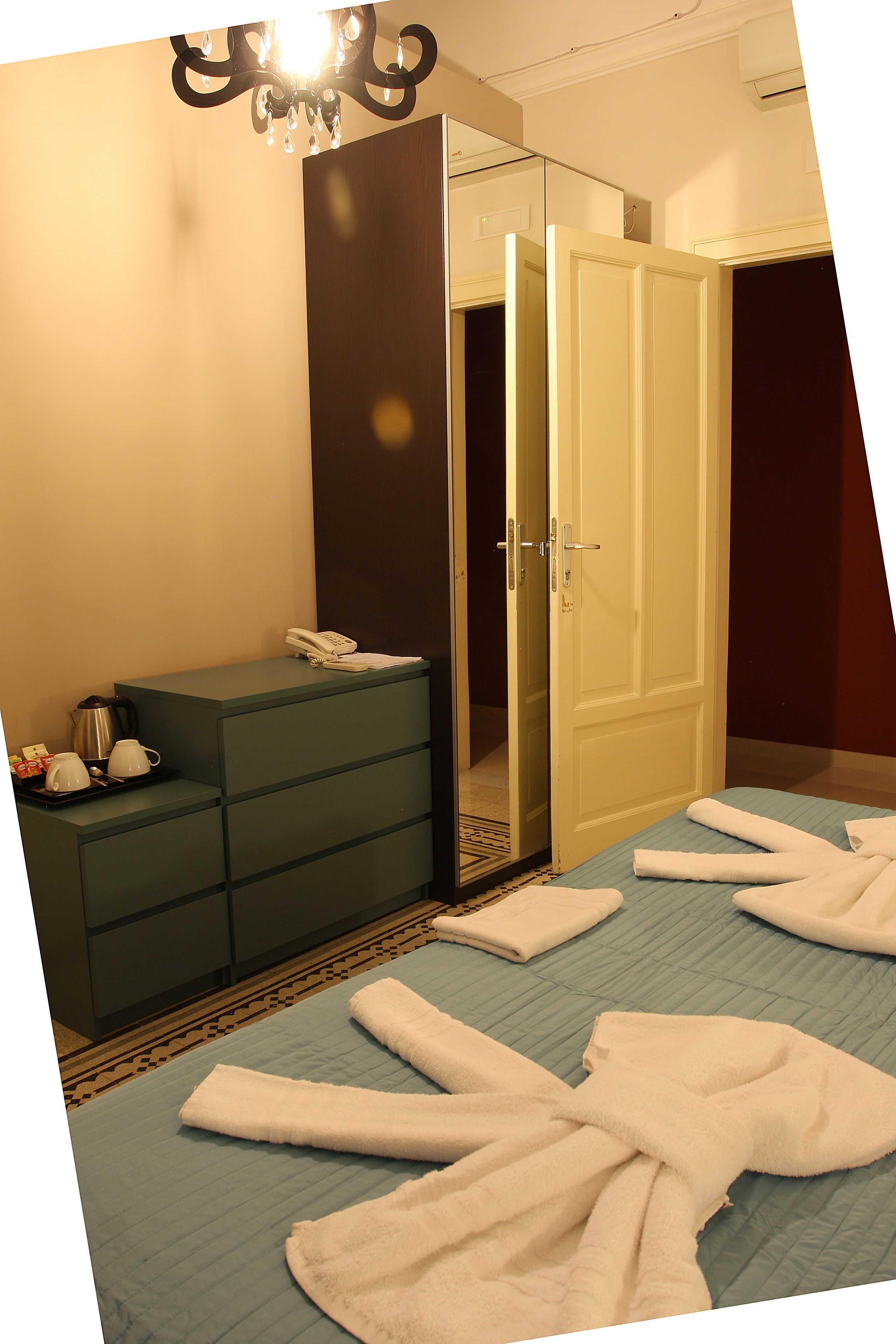 A hotel room with a bed, a dresser, a mirror, and a chandelier.