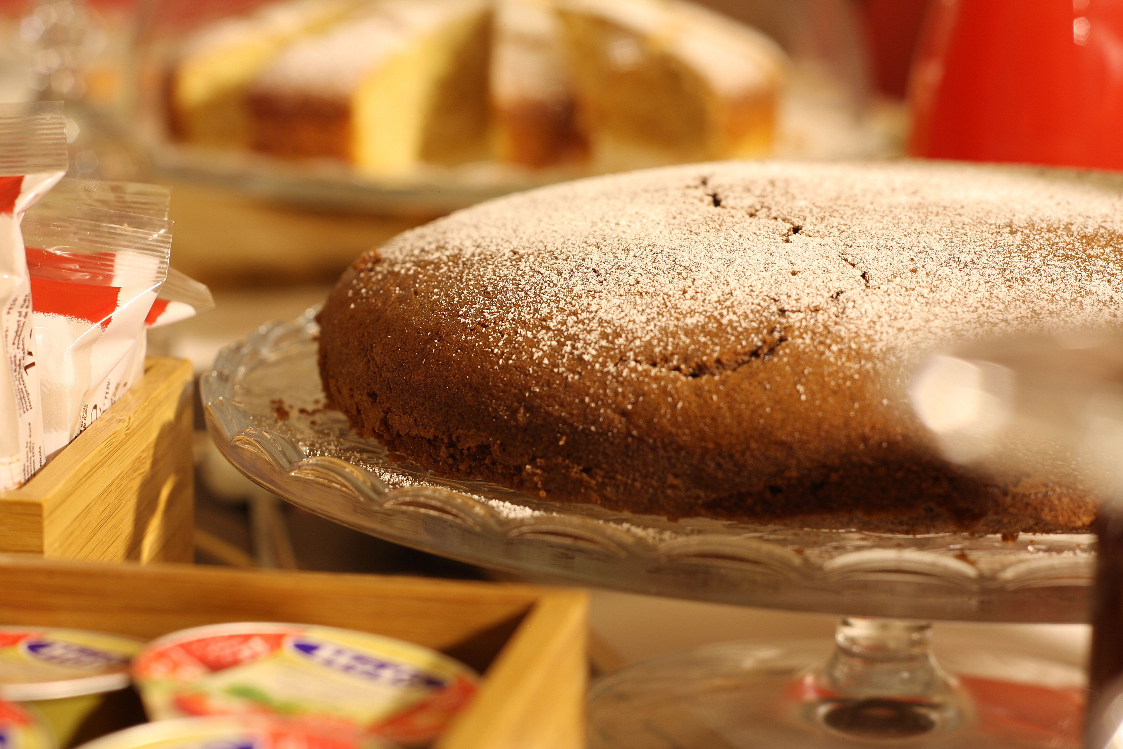 A cake on a glass stand with a dusting of powdered sugar on top.