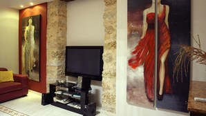 A living room with a flat-screen TV, a red sofa, and two large paintings on the walls. - Abatellis Luxury (Palermo)