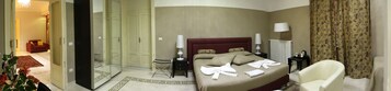 A hotel room with a bed, a sitting area with a chair, a small table with a lamp, a radiator, and a mirror.