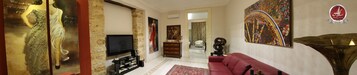 Un soggiorno con televisore, un divano rosso, un tappeto decorativo e un quadro di grandi dimensioni appeso al muro.