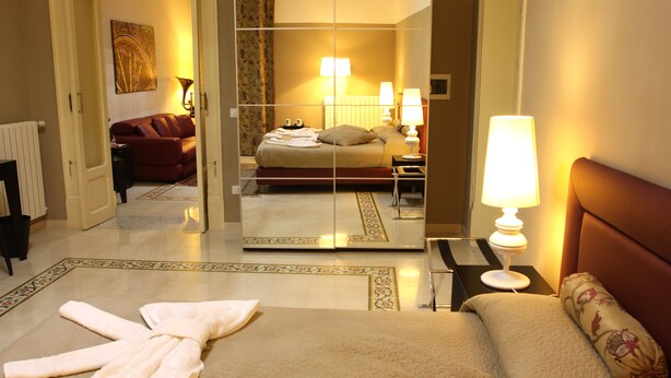 A hotel room with a bed, a sitting area, a mirror, and a bathroom visible through an open door. - Abatellis Luxury (Palermo)