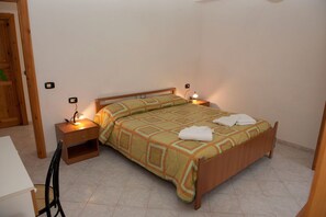 A single-bed room with a wooden headboard, a bedside table with a lamp, and a chair.