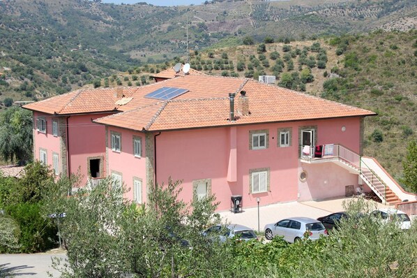 A pink building with a tiled roof, solar panels, and a staircase leading to a balcony.