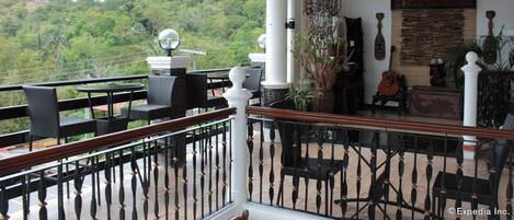 A balcony with outdoor furniture, a chandelier, and a view of a forested area.