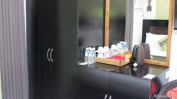 A black wardrobe with a mirror, a small table with toiletries, and a bed with a headboard and pillows.