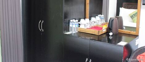 Un armadio nero con uno specchio, un tavolino con articoli da toilette e un letto con testiera e cuscini.