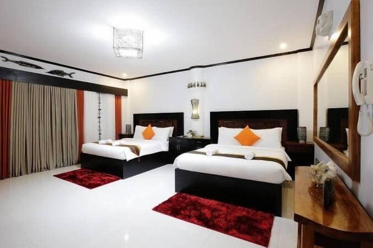 A hotel room with two beds, a large mirror, and a red rug.