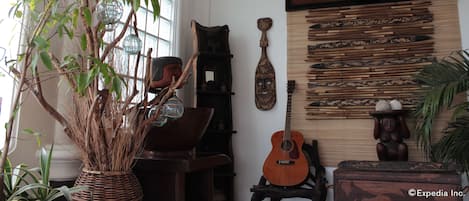 A room with a large window, a wooden guitar, a decorative mask, and a wall with wooden carvings.