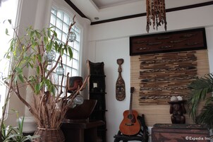 Ein Zimmer mit großem Fenster, einer Holzgitarre, einer Zierde-Maske und einer Wand mit Holzschnitzereien.