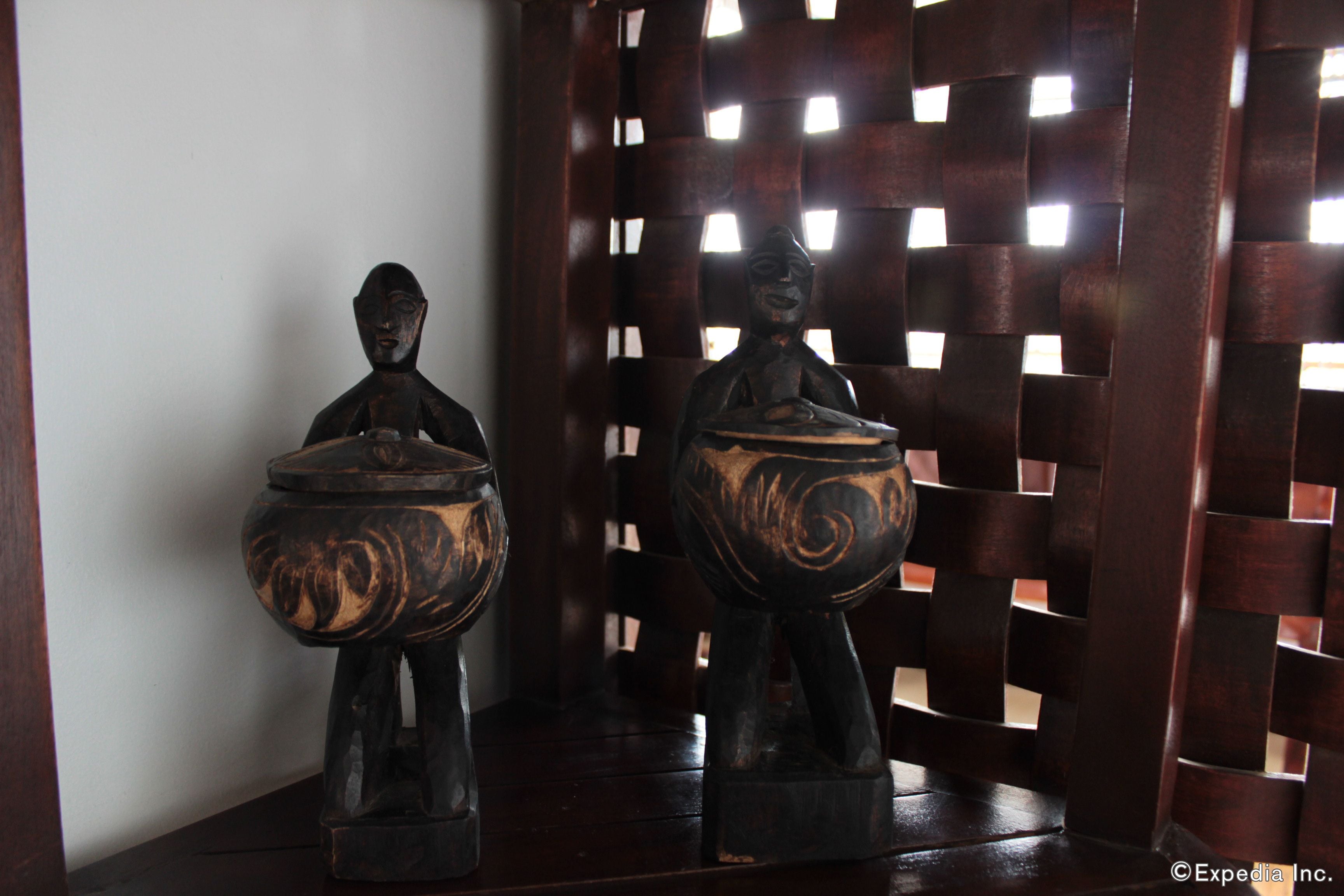 Two wooden sculptures with bowls, placed on a dark wooden surface against a lattice backdrop.