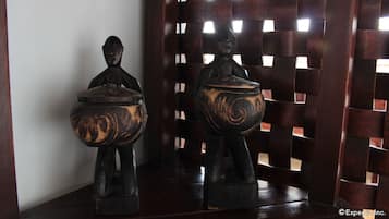 Deux sculptures en bois, chacune surmontée d’un bol, sont disposées sur une surface en bois sombre, le tout se détachant sur un fond en treillis.