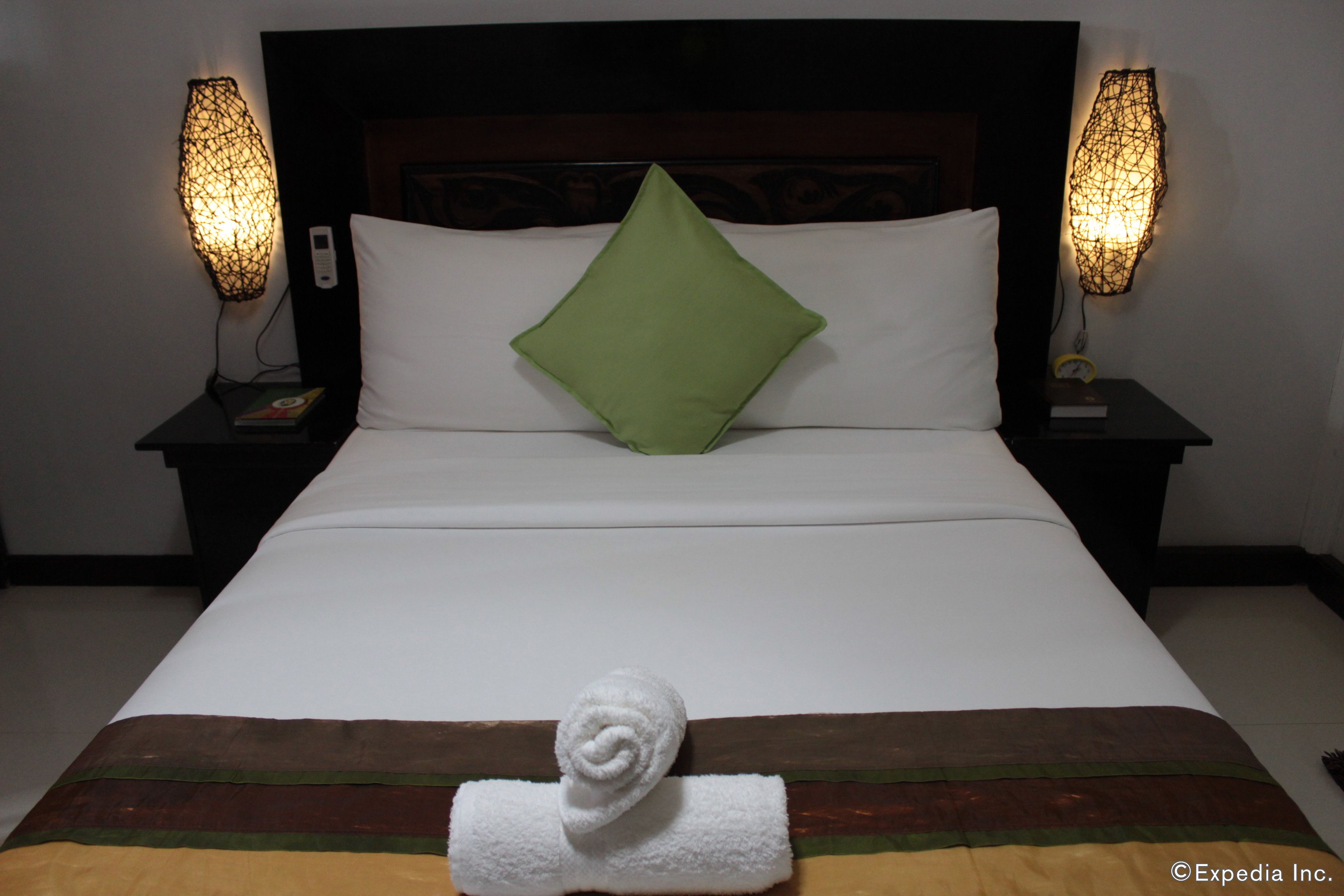 A neatly made bed with a green pillow, white bedding, and a rolled towel on the bed.