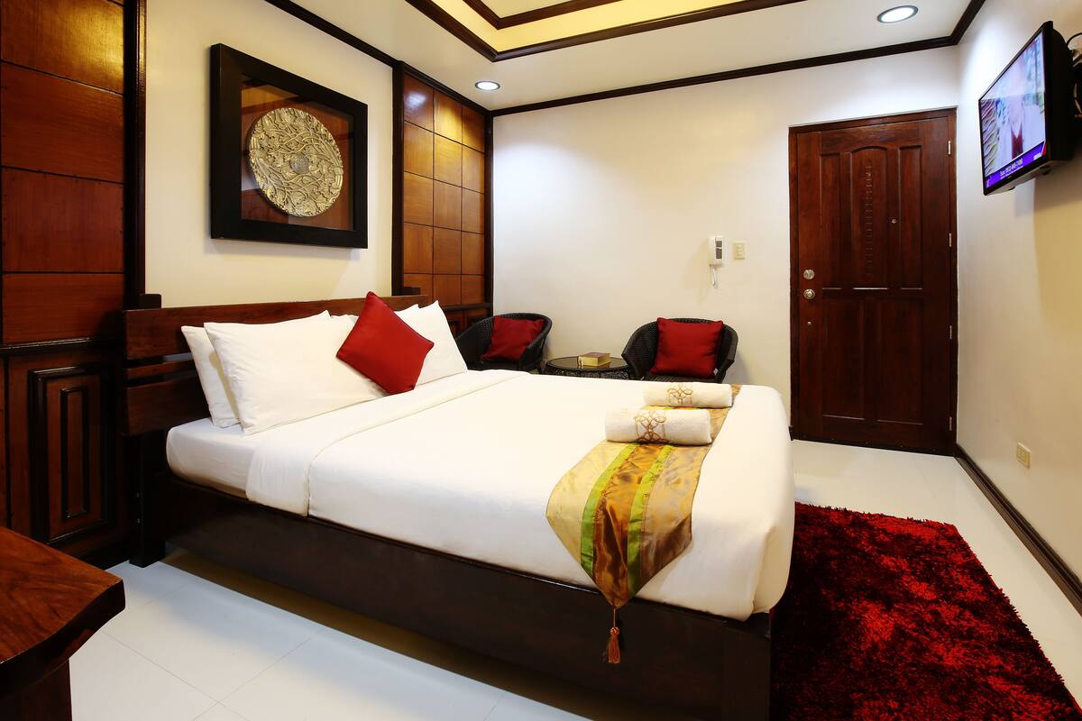 A neatly arranged bedroom with a bed, a small table, and a TV mounted on the wall.