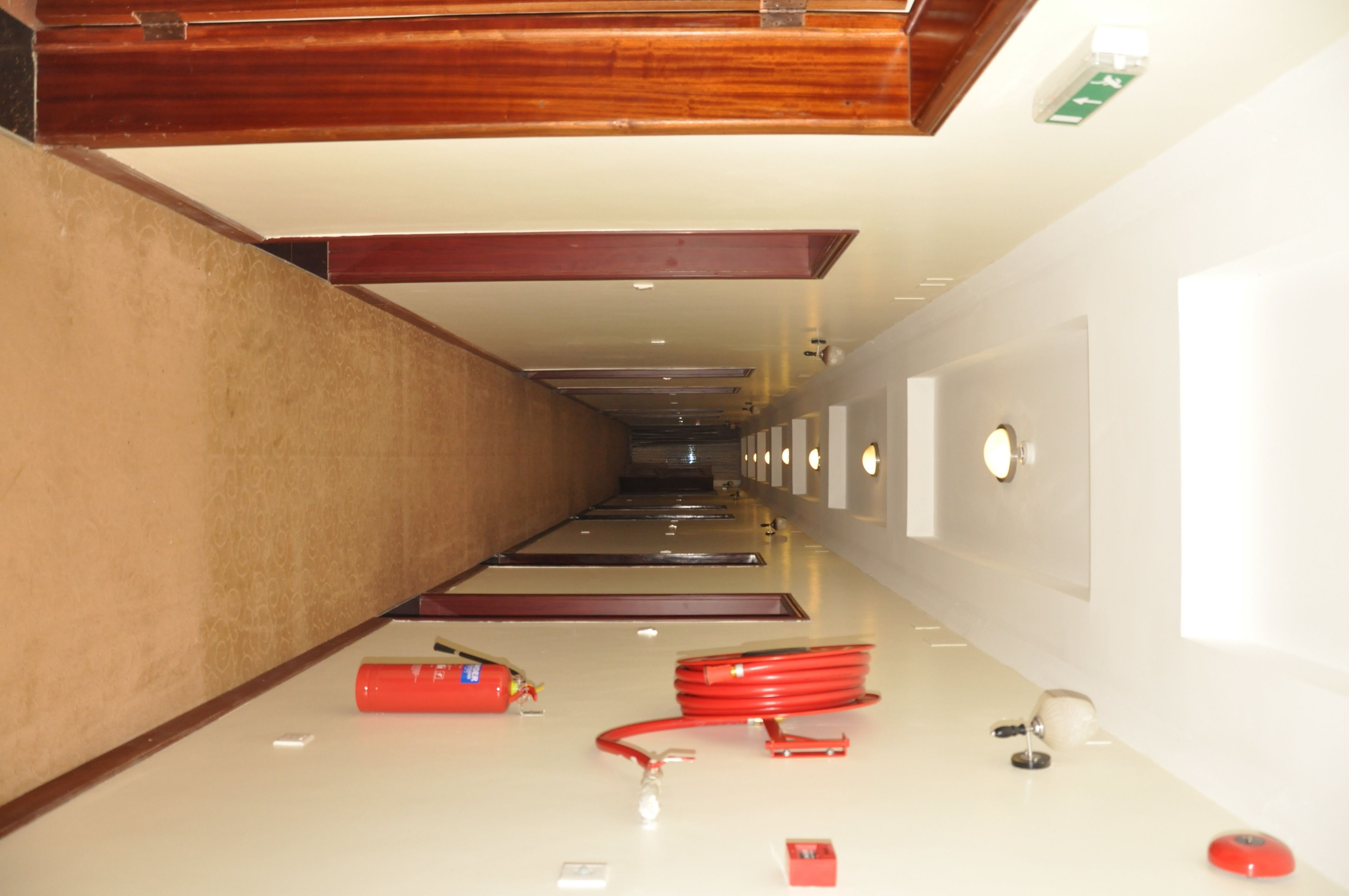 Un couloir d’hôtel avec un plafond en bois, un extincteur et un tuyau rouge sur le sol.
