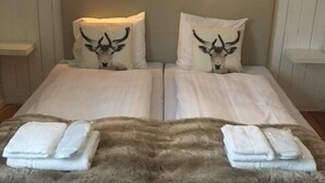 A double bed with two pillows featuring a bull's head design, a fluffy brown rug, and two bedside tables with lamps. - Sonfjällsgården Wärdshus & Hotell (Hede)
