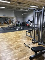 Un gimnasio con suelo de madera, equipamiento de levantamiento de pesas y un espejo en la pared.