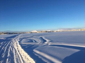A vast, open snowy landscape with tire tracks leading into the distance and a clear blue sky above. - Sonfjällsgården Wärdshus & Hotell (Hede)
