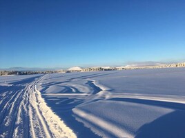 Un paisaje nevado y extenso con surcos de neumáticos que se adentran en la distancia y un cielo azul despejado arriba.