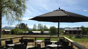 An outdoor patio with tables and chairs, a large umbrella, and a view of a rural landscape with buildings and mountains in the background. - Sonfjällsgården Wärdshus & Hotell (Hede)
