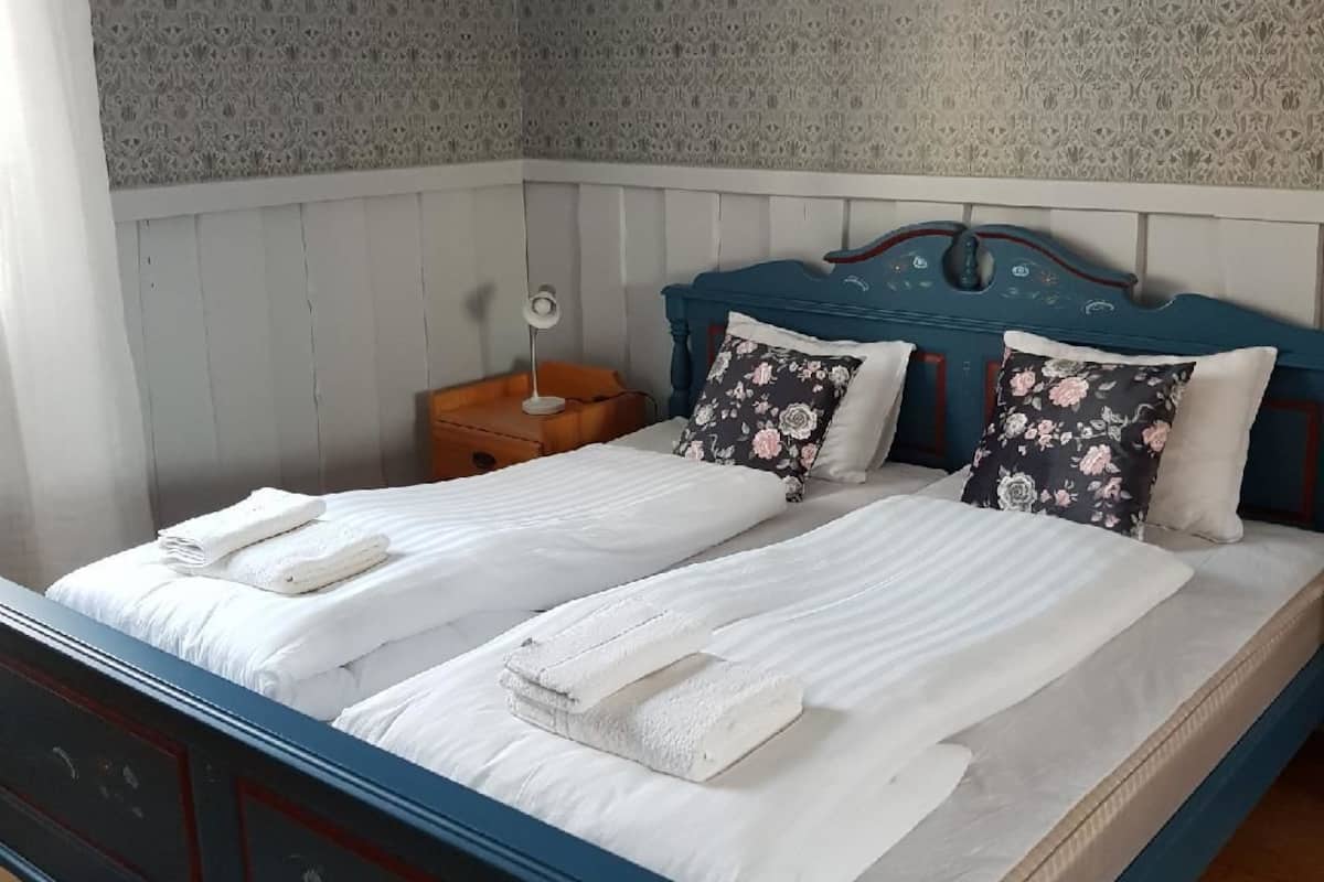 A bedroom with a blue bed frame, white bedding, floral pillows, and a patterned wallpaper.