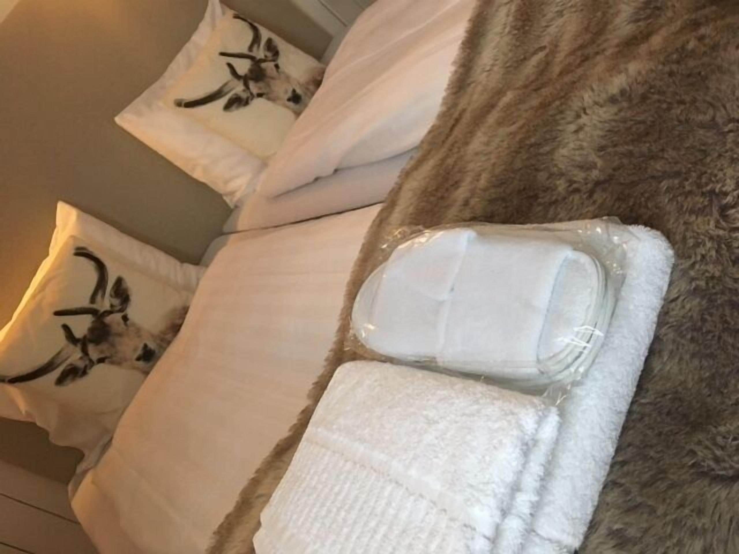Una cama con un almohadón blanco que tiene un diseño negro, una toalla blanca y un envoltorio de plástico.
