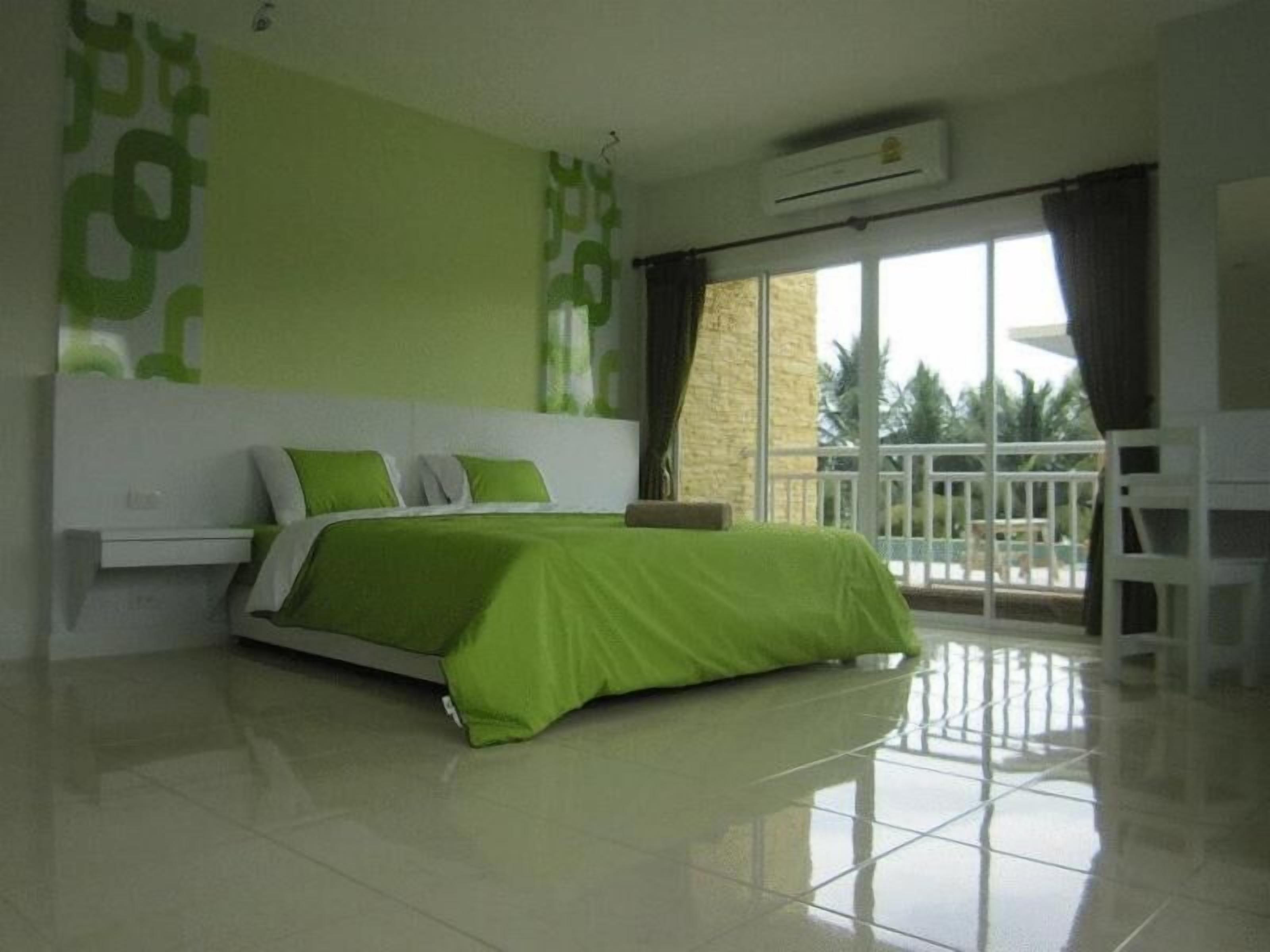 Een slaapkamer met een groen beddengoed, een witte nachtkastje en een balkon met een witte balustrade.