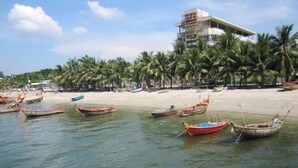 Una playa con varias embarcaciones ancladas en el agua, una orilla arenosa y un edificio en construcción al fondo.