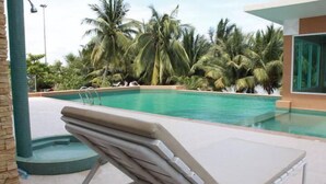 Un área de piscina con una tumbona, palmeras y una piscina azul cristalina.